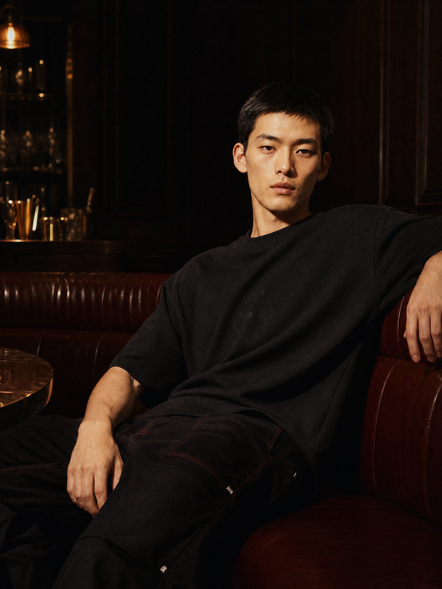 Man in black oversized t-shirt seated in a dark bar — Weezy Night Out menswear collection